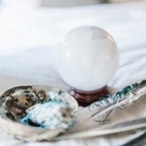 Crystal ball and feather with smudging tools on a soft surface, ideal for spiritual and mystical themes.