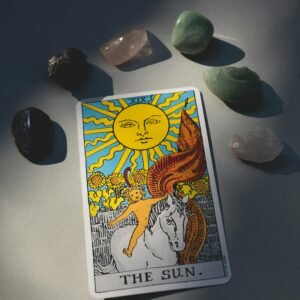 A tarot card titled 'The Sun' surrounded by various healing crystals, illuminated by sunlight.