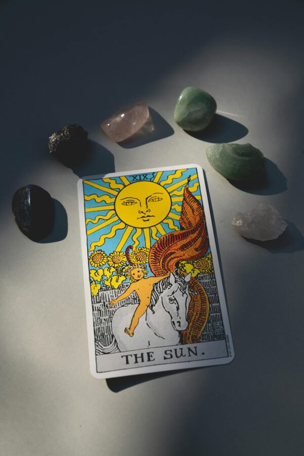 A tarot card titled 'The Sun' surrounded by various healing crystals, illuminated by sunlight.